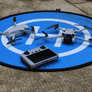Two drones and control device on landing pad.