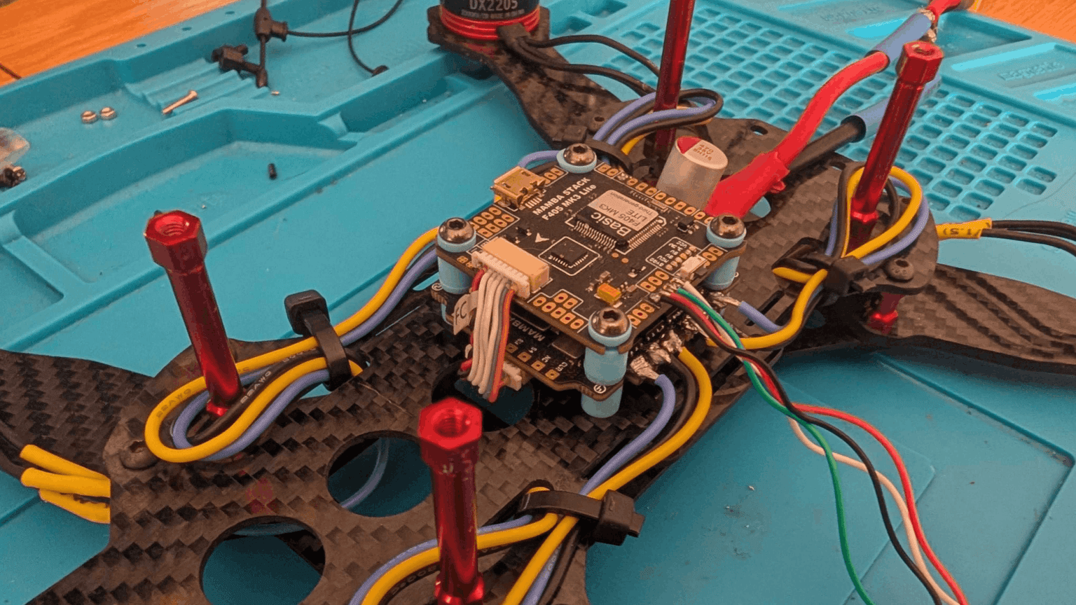 Close-up of FPV drone on workbench, showing exposed wiring, DJI O3 Air Unit, and flight controller stack.